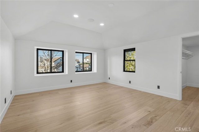 unfurnished bedroom with lofted ceiling, light wood-style flooring, baseboards, and a walk in closet