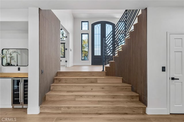 foyer entrance with stairs, beverage cooler, baseboards, and wood finished floors