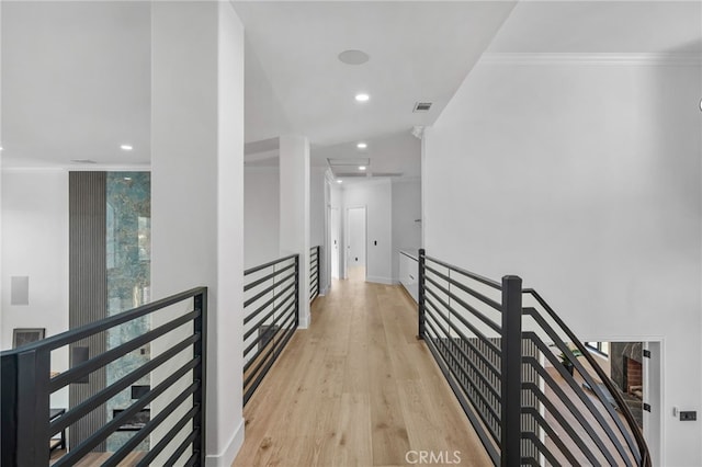 hall with recessed lighting, visible vents, light wood-style flooring, ornamental molding, and an upstairs landing