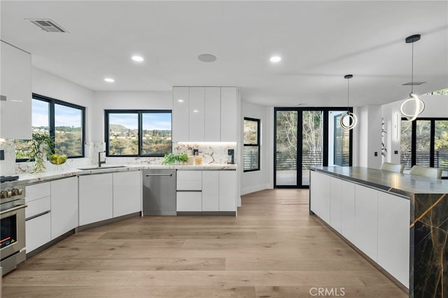 kitchen with stainless steel appliances, modern cabinets, white cabinets, and decorative light fixtures