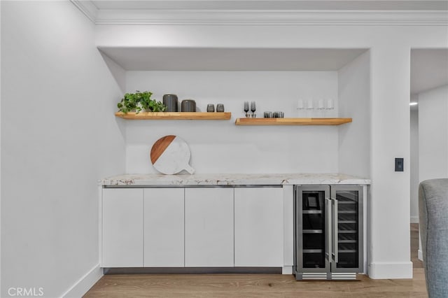 bar featuring wine cooler, crown molding, light wood-style flooring, a bar, and baseboards