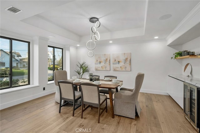 dining room with baseboards, visible vents, a raised ceiling, light wood-style flooring, and crown molding