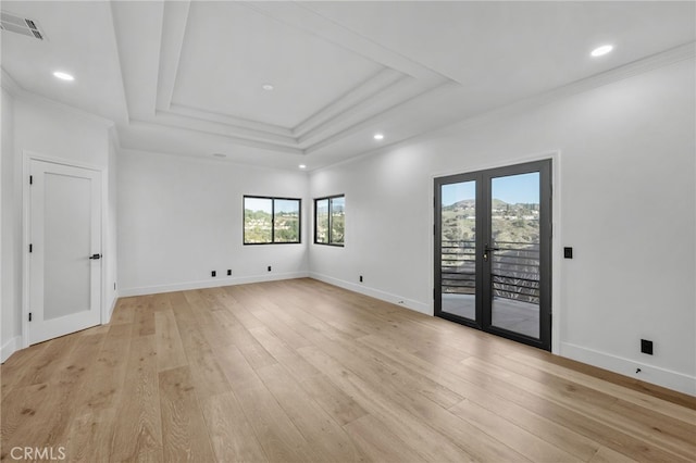 empty room featuring light wood-style flooring, visible vents, baseboards, a raised ceiling, and crown molding