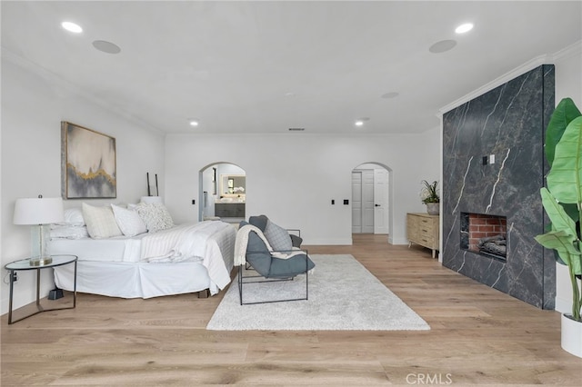 bedroom featuring light wood-style floors, arched walkways, a fireplace, and ornamental molding