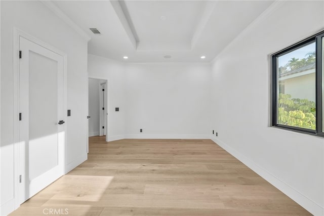 spare room with visible vents, baseboards, light wood-style floors, ornamental molding, and a raised ceiling