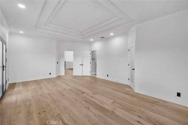 spare room featuring light wood-type flooring, a raised ceiling, crown molding, and baseboards