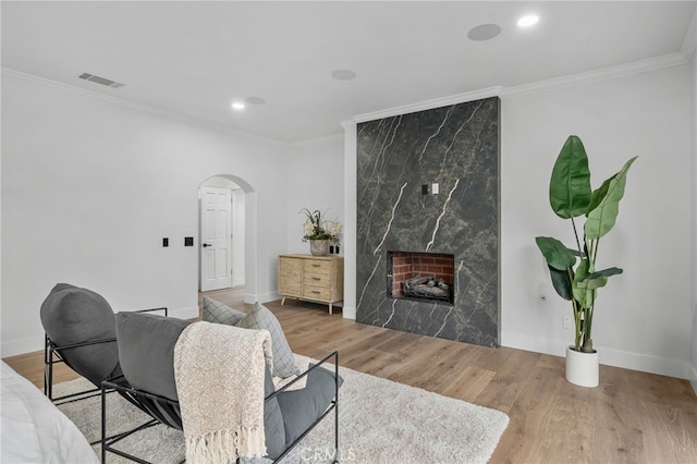 living area featuring arched walkways, crown molding, visible vents, a high end fireplace, and wood finished floors