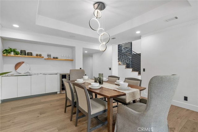 dining room featuring crown molding, a raised ceiling, visible vents, light wood-type flooring, and baseboards