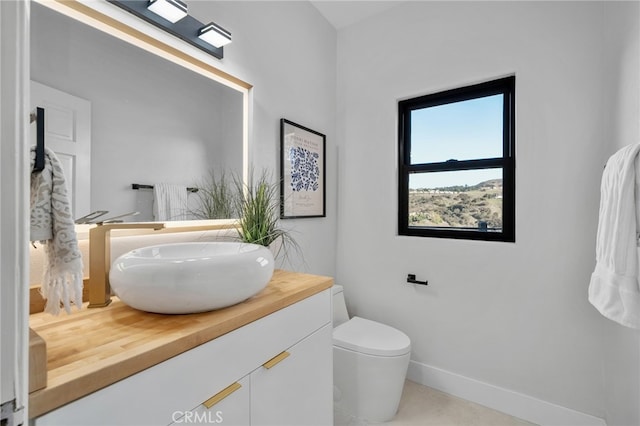 half bathroom with baseboards, vanity, and toilet