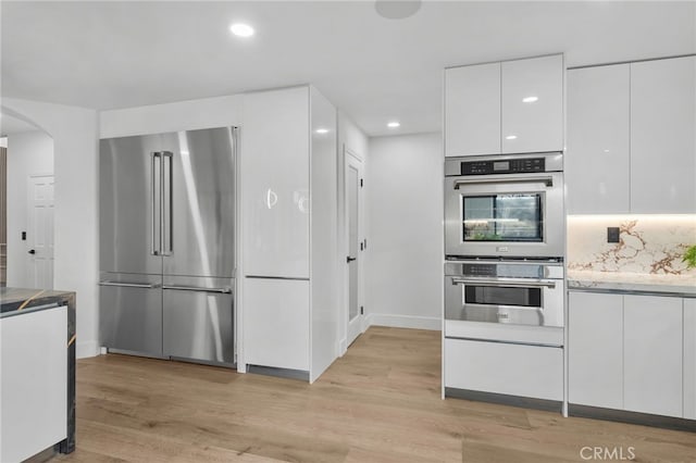 kitchen with arched walkways, white cabinets, light wood-style flooring, modern cabinets, and stainless steel appliances