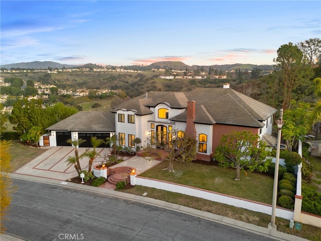 french country home with driveway, an attached garage, a mountain view, and a lawn