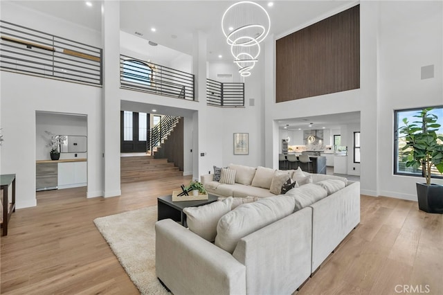 living room featuring baseboards, light wood-style floors, stairway, and an inviting chandelier