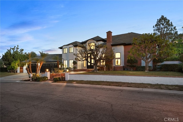 french country inspired facade featuring concrete driveway, a chimney, an attached garage, and stucco siding