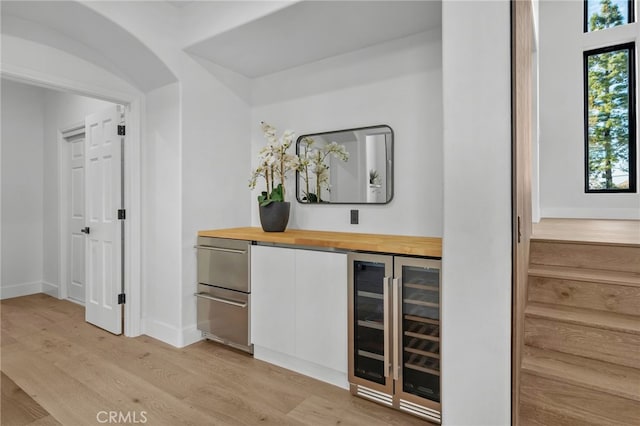 bar featuring arched walkways, beverage cooler, light wood-style flooring, and baseboards