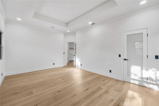 spare room featuring light wood finished floors, visible vents, a raised ceiling, and crown molding