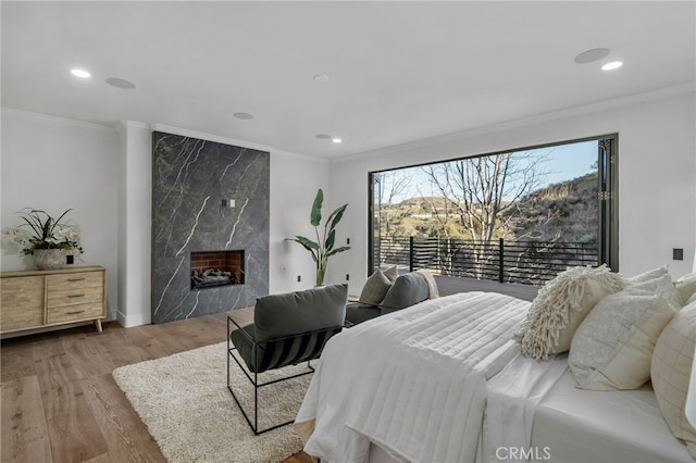 bedroom featuring a premium fireplace, ornamental molding, and wood finished floors