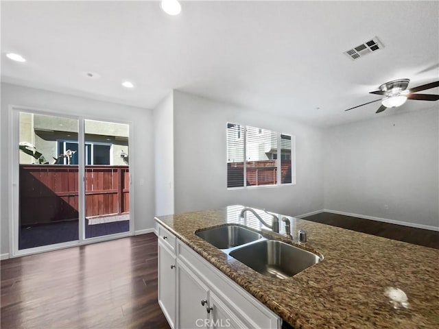 kitchen with a sink, dark wood finished floors, visible vents, white cabinets, and dark stone counters