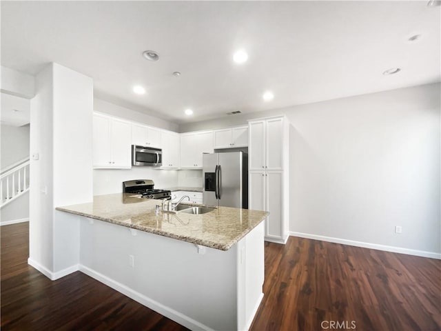kitchen featuring light stone counters, a sink, a peninsula, stainless steel appliances, and dark wood-type flooring