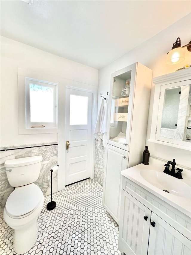 bathroom featuring wainscoting, tile walls, toilet, and vanity