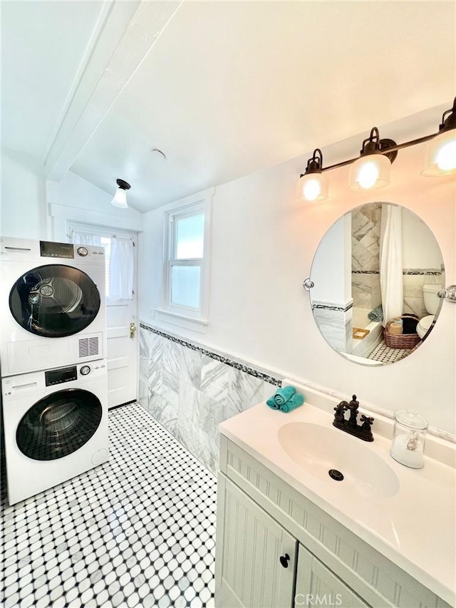 interior space featuring stacked washer and dryer, laundry area, tile walls, wainscoting, and a sink