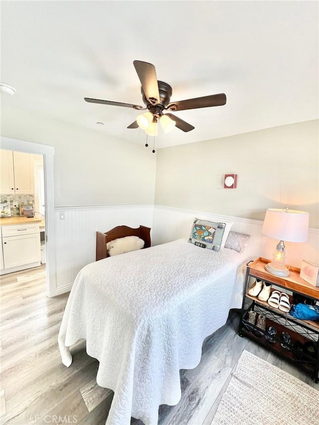 bedroom with light wood-style flooring, ceiling fan, and wainscoting