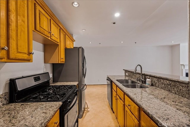 kitchen featuring brown cabinetry, light stone counters, stainless steel appliances, and a sink