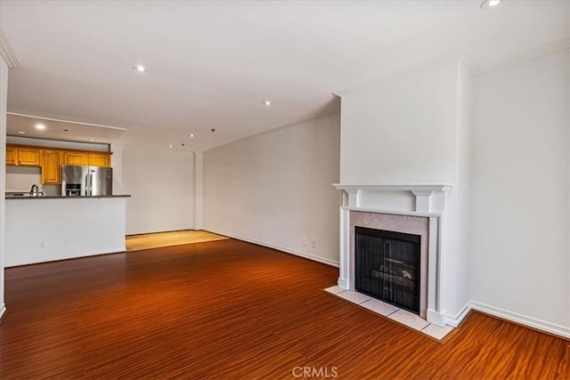 unfurnished living room with light wood finished floors, baseboards, a fireplace with flush hearth, ornamental molding, and recessed lighting