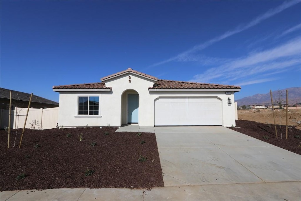 mediterranean / spanish home featuring stucco siding, concrete driveway, an attached garage, a mountain view, and fence