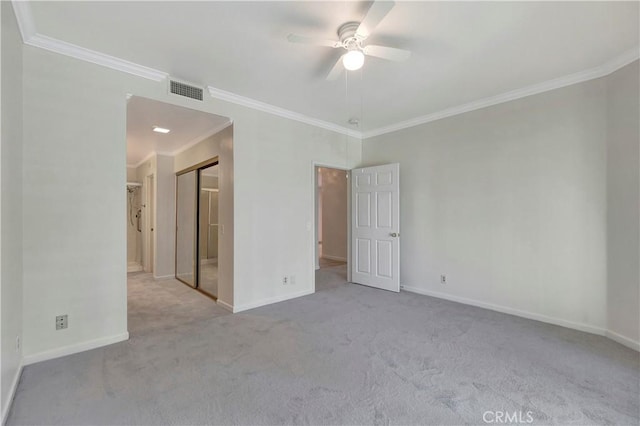 empty room with ceiling fan, light colored carpet, visible vents, baseboards, and crown molding