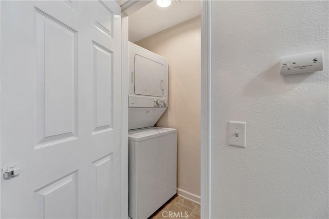 clothes washing area with light tile patterned floors, stacked washer and dryer, laundry area, and baseboards