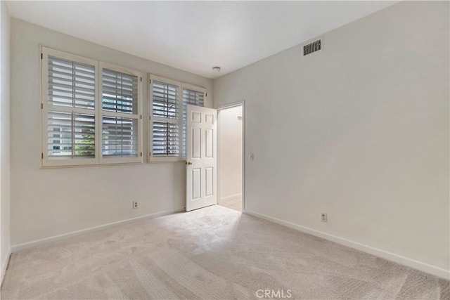 empty room with visible vents, light carpet, and baseboards