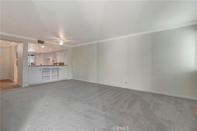 unfurnished living room featuring baseboards, ornamental molding, ceiling fan, and light colored carpet