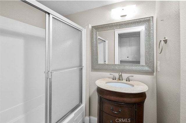 bathroom with a textured wall, bath / shower combo with glass door, and vanity