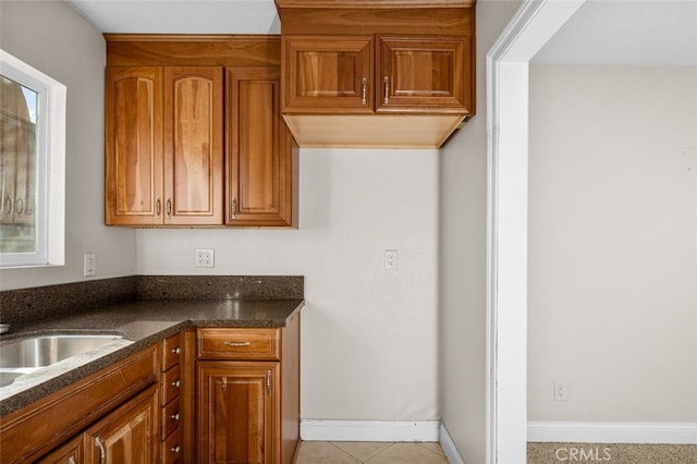 kitchen with dark stone countertops, brown cabinetry, light tile patterned flooring, and baseboards