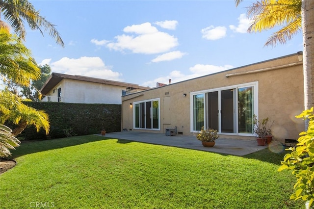 rear view of house with a patio area, a lawn, and stucco siding