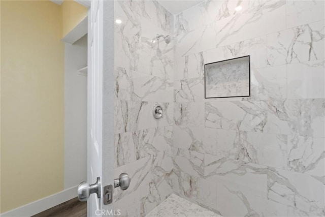 full bath featuring baseboards, tiled shower, and wood finished floors