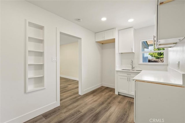 kitchen with white cabinets, wood finished floors, baseboards, and a sink