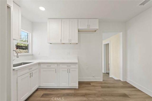 kitchen with visible vents, white cabinetry, light wood-style floors, and a sink