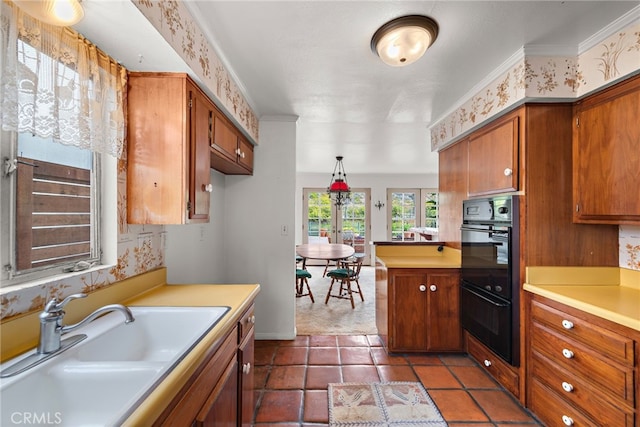 kitchen with light countertops, a sink, dobule oven black, a peninsula, and brown cabinetry