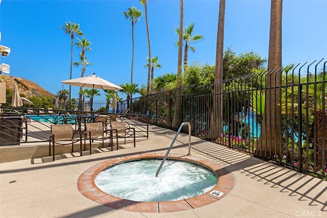 pool featuring a community hot tub, a patio area, fence, and a mountain view