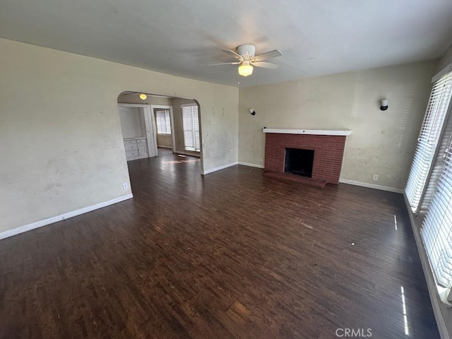 unfurnished living room featuring arched walkways, a fireplace, dark wood finished floors, and baseboards