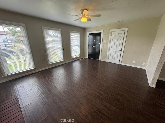 empty room with a healthy amount of sunlight, a ceiling fan, baseboards, and dark wood-style flooring