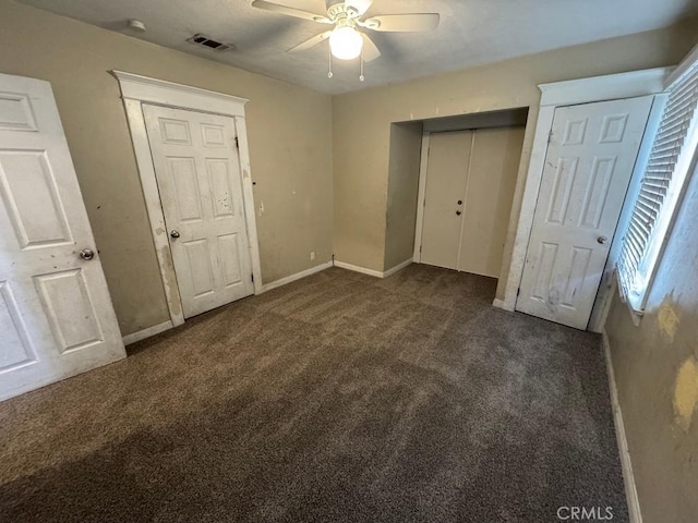 unfurnished bedroom with visible vents, baseboards, a ceiling fan, dark carpet, and two closets