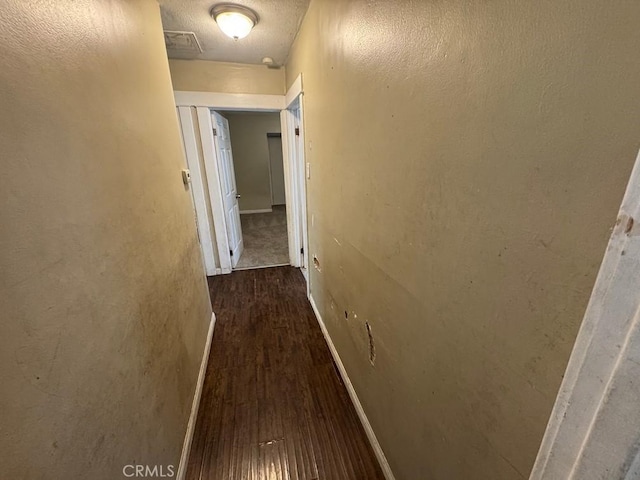 hall featuring a textured ceiling, baseboards, and dark wood-style flooring