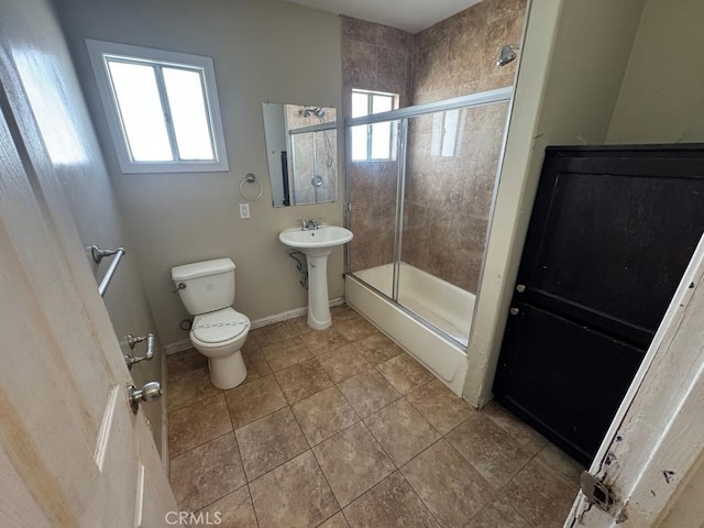 bathroom featuring baseboards, toilet, tile patterned flooring, combined bath / shower with glass door, and a sink