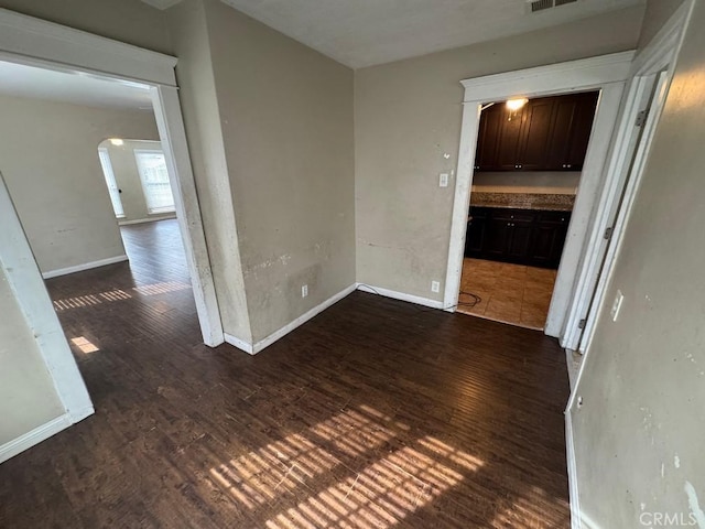 interior space with dark wood-style floors, baseboards, visible vents, and arched walkways