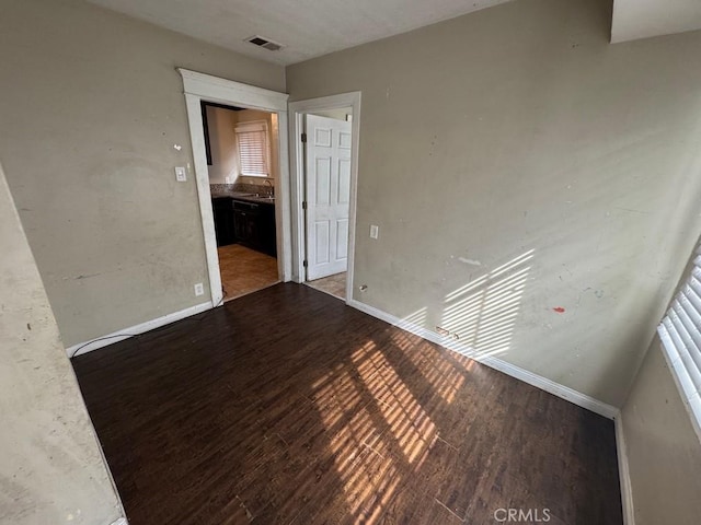 empty room featuring a sink, wood finished floors, visible vents, and baseboards