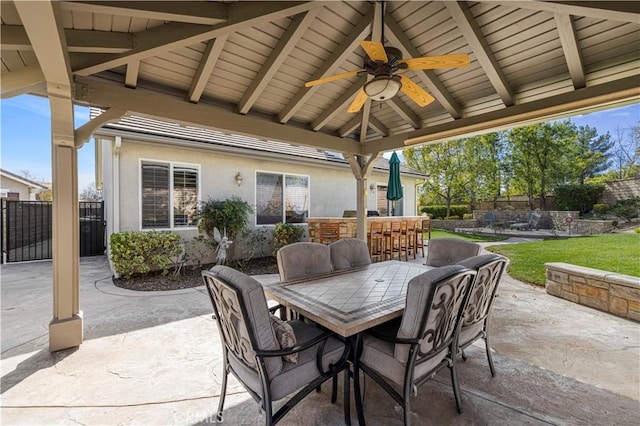 view of patio featuring a ceiling fan, outdoor dry bar, fence, outdoor dining area, and a gazebo