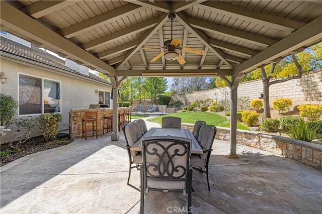 view of patio featuring a fenced backyard, a ceiling fan, outdoor dry bar, a gazebo, and outdoor dining space