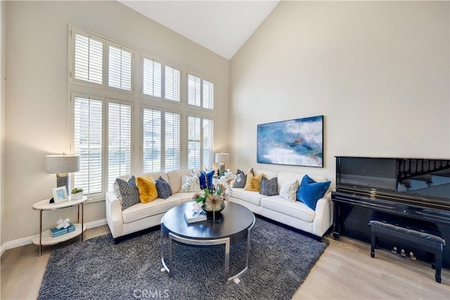 living room featuring high vaulted ceiling, baseboards, and wood finished floors